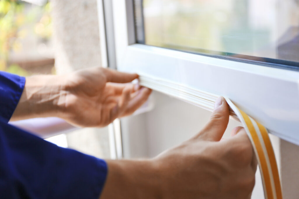 Construction worker putting sealing foam tape on window in house. Evenly Heat Multiple Stories