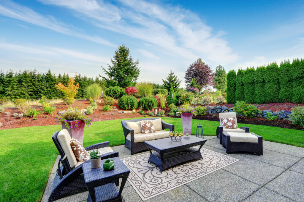 Impressive backyard landscape design. Cozy patio area with settees and table. Patio Ready for Summer